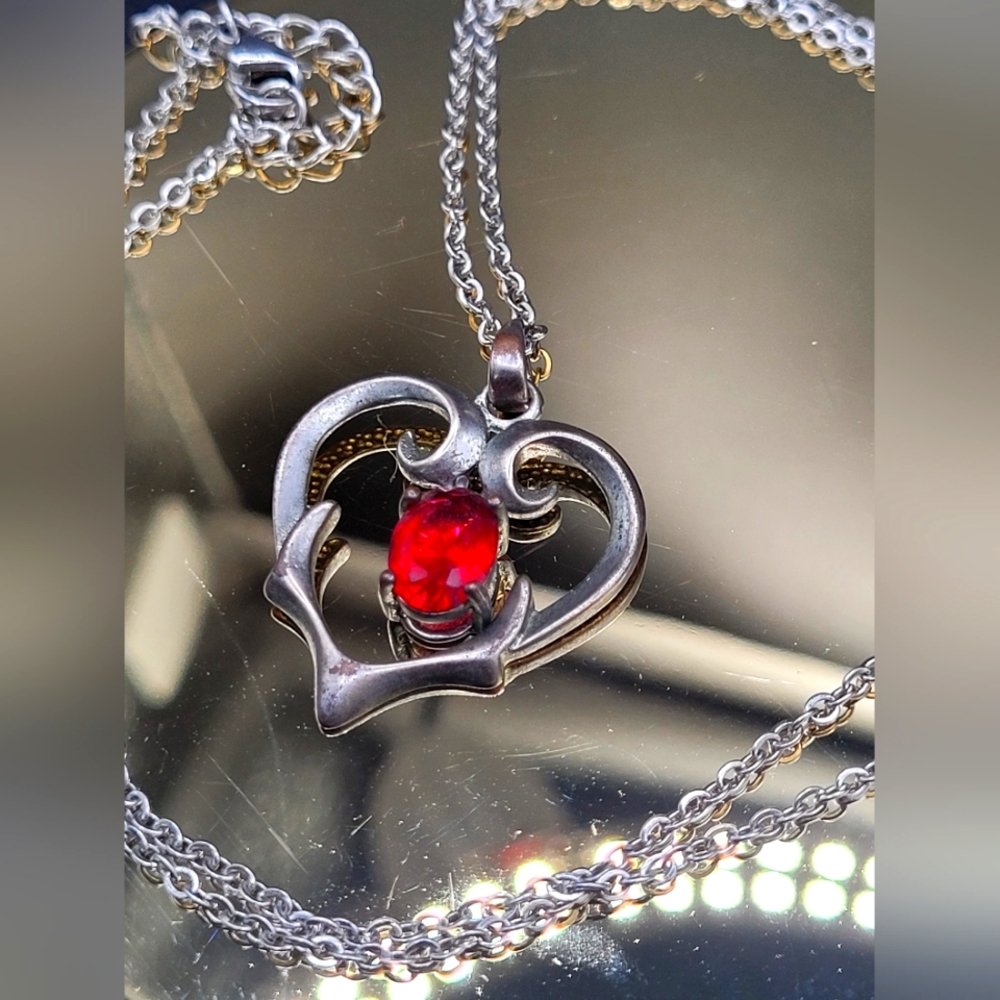Silver heart pendant necklace with red gemstone.